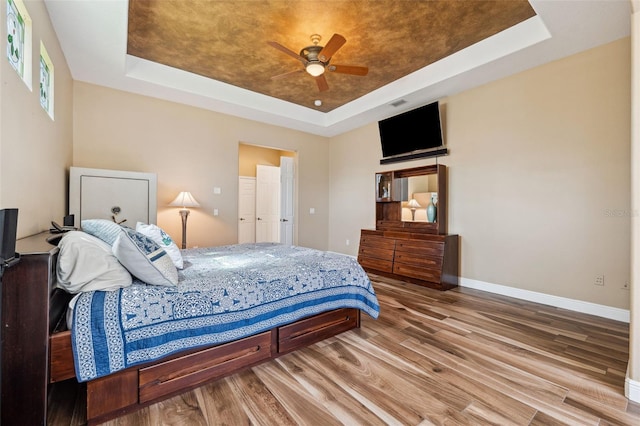 bedroom with a tray ceiling, ceiling fan, and hardwood / wood-style flooring