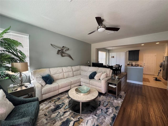 living room featuring a healthy amount of sunlight, dark wood-type flooring, a textured ceiling, and ceiling fan