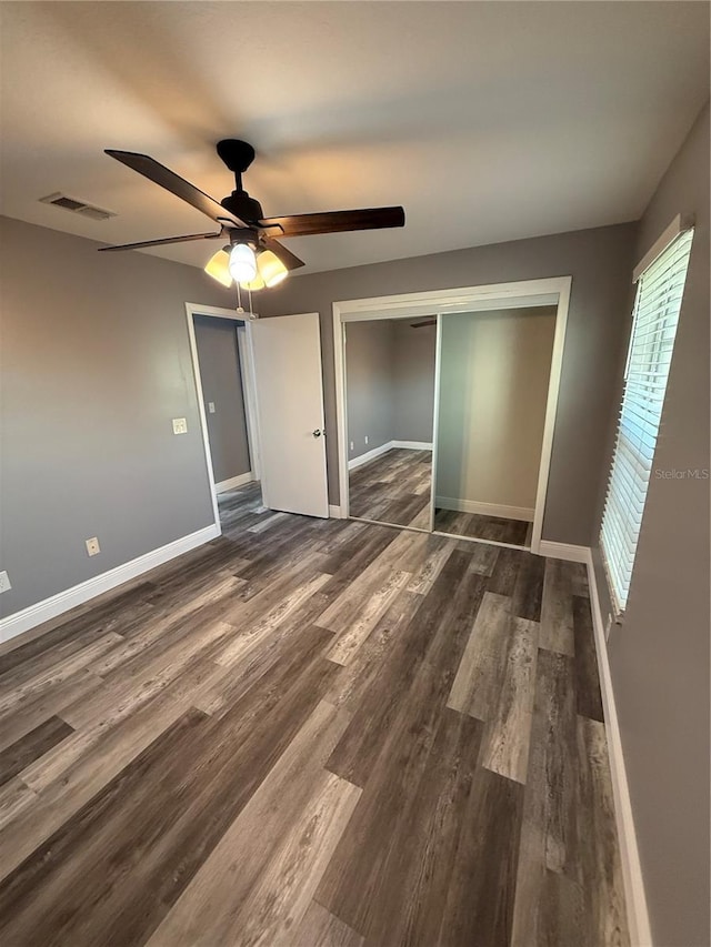 unfurnished bedroom featuring baseboards, visible vents, dark wood-style floors, multiple windows, and a closet