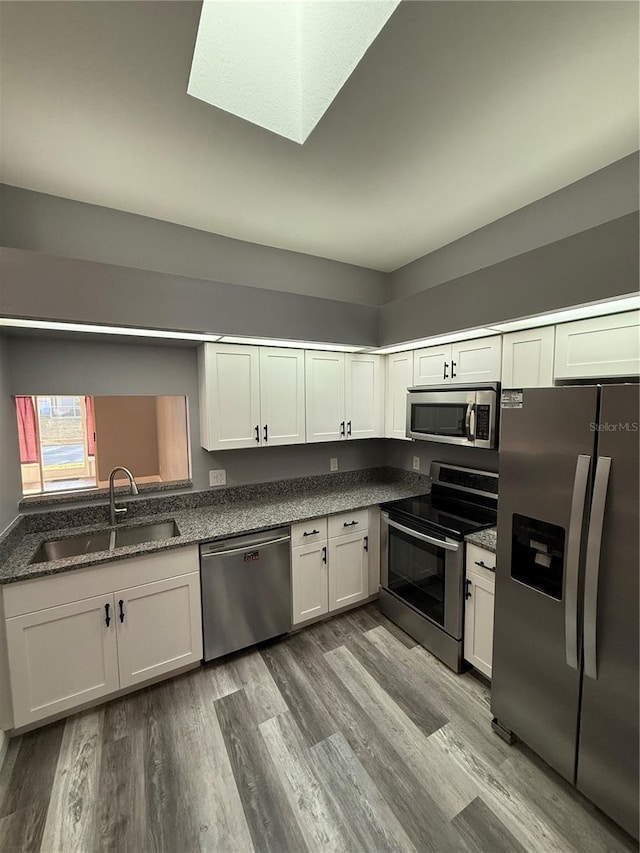 kitchen featuring dark stone counters, stainless steel appliances, light wood-type flooring, white cabinetry, and a sink