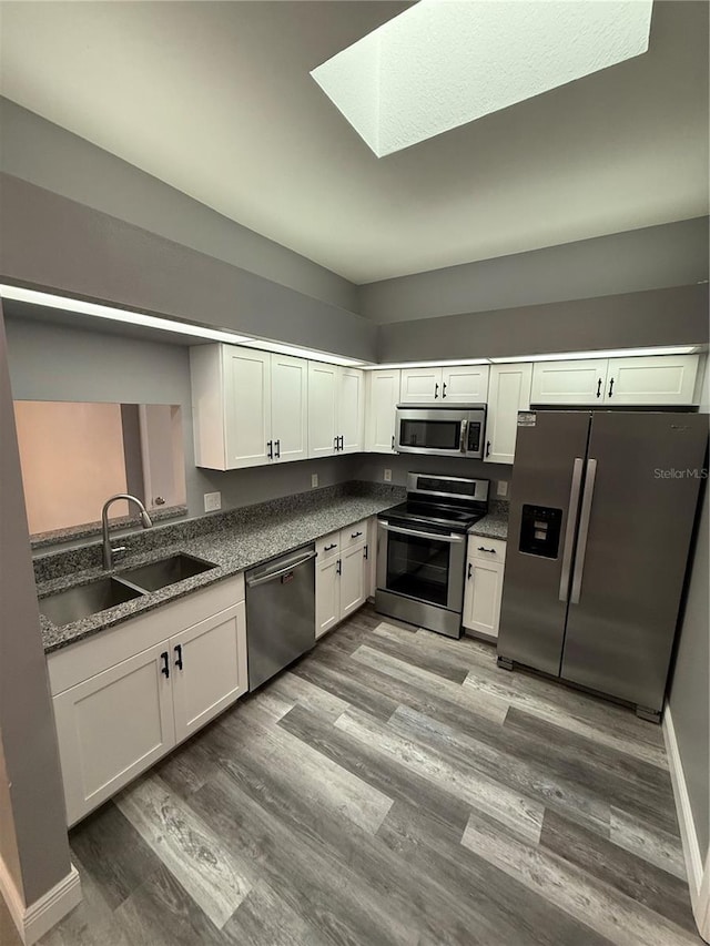 kitchen featuring hardwood / wood-style floors, a skylight, sink, white cabinets, and stainless steel appliances