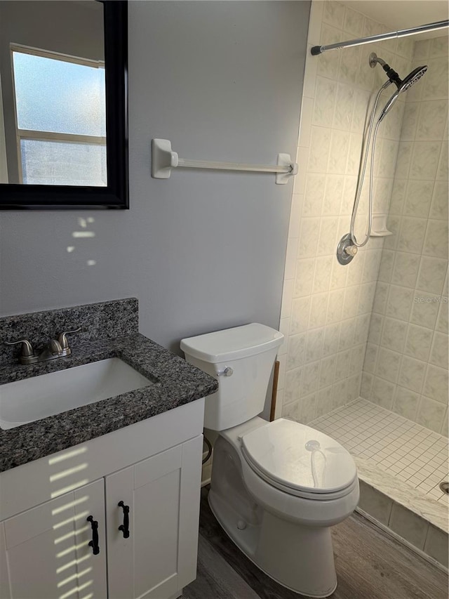 bathroom with hardwood / wood-style flooring, vanity, toilet, and a tile shower