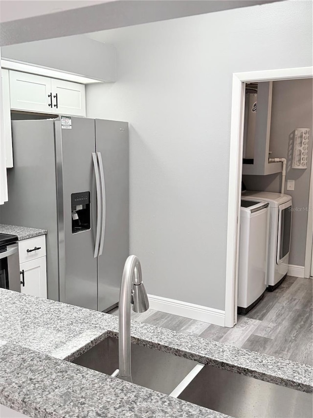 4218 San Rafael Ave, New Port Richey, FL 34655 - kitchen with white cabinetry, light stone countertops, stainless steel refrigerator with ice dispenser, independent washer and dryer, and light wood-style floors
