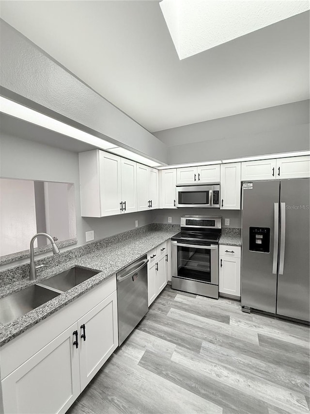 4218 San Rafael Ave, New Port Richey, FL 34655 - kitchen with stainless steel appliances, a sink, white cabinets, light stone counters, and light wood-type flooring