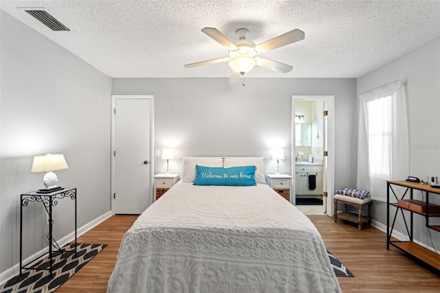 bedroom with ceiling fan, ensuite bathroom, a textured ceiling, and light wood-type flooring