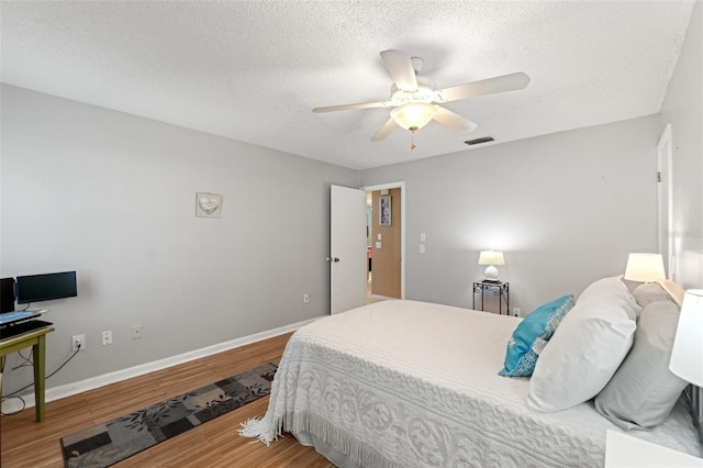 bedroom with ceiling fan, wood-type flooring, and a textured ceiling