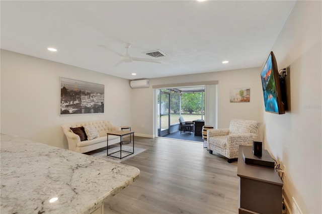 living room with ceiling fan, hardwood / wood-style floors, and a wall unit AC