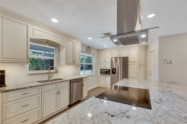 kitchen with sink, light stone counters, island exhaust hood, stainless steel appliances, and cream cabinetry