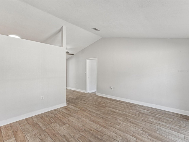 unfurnished room with vaulted ceiling, a textured ceiling, and light hardwood / wood-style flooring