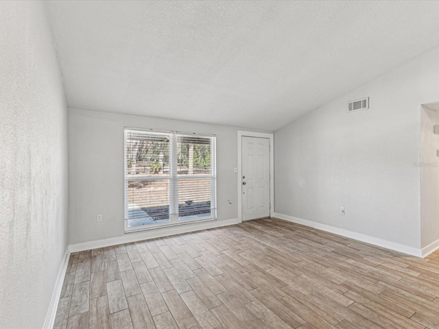 empty room with vaulted ceiling, light hardwood / wood-style floors, and a textured ceiling