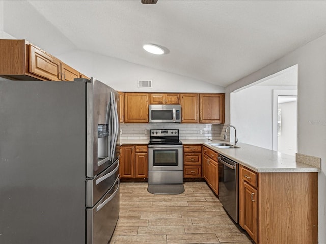 kitchen featuring lofted ceiling, sink, appliances with stainless steel finishes, kitchen peninsula, and backsplash