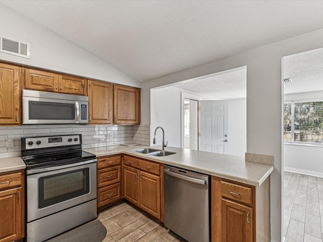 kitchen featuring sink, vaulted ceiling, appliances with stainless steel finishes, kitchen peninsula, and decorative backsplash