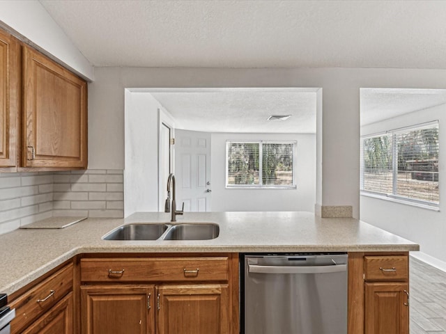 kitchen with sink, backsplash, a textured ceiling, stainless steel dishwasher, and kitchen peninsula