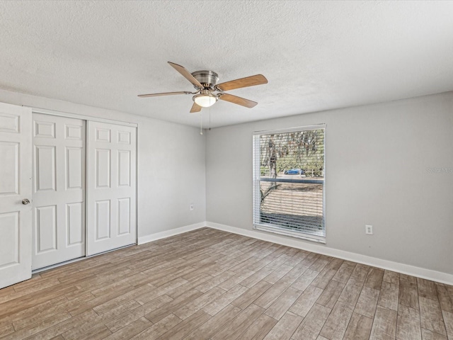 unfurnished bedroom featuring ceiling fan, a textured ceiling, a closet, and light wood-type flooring