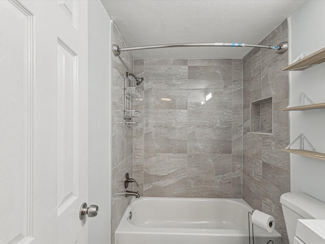 bathroom with a textured ceiling, toilet, and tiled shower / bath