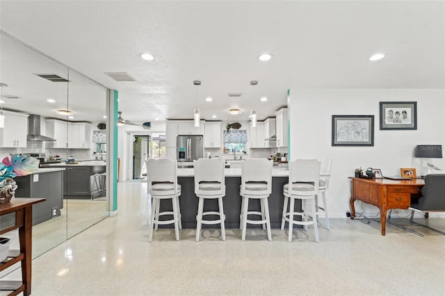 kitchen with wall chimney exhaust hood, white cabinetry, appliances with stainless steel finishes, a kitchen breakfast bar, and pendant lighting