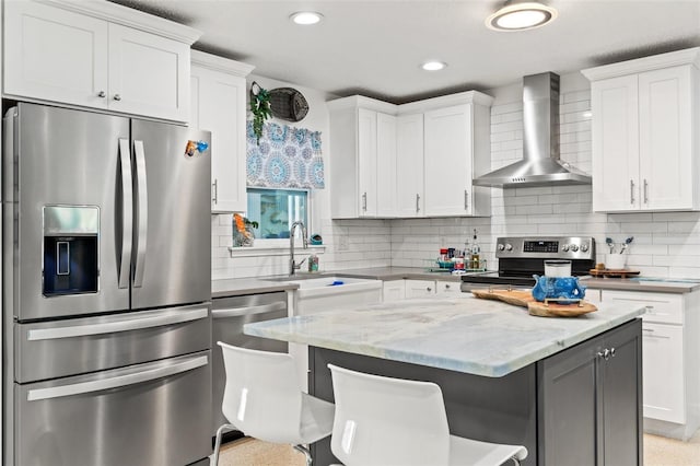 kitchen with wall chimney exhaust hood, sink, a breakfast bar area, appliances with stainless steel finishes, and white cabinets