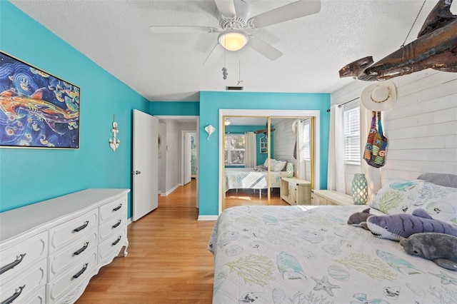 bedroom featuring ceiling fan, wooden walls, a textured ceiling, a closet, and light wood-type flooring