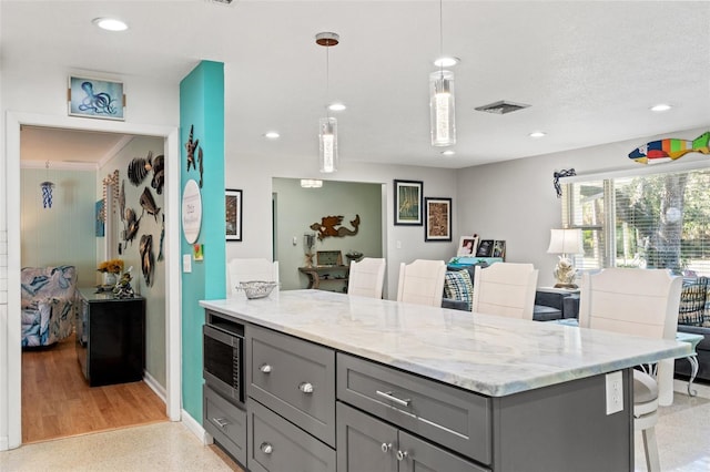 kitchen with gray cabinets, a breakfast bar area, hanging light fixtures, light stone counters, and a textured ceiling