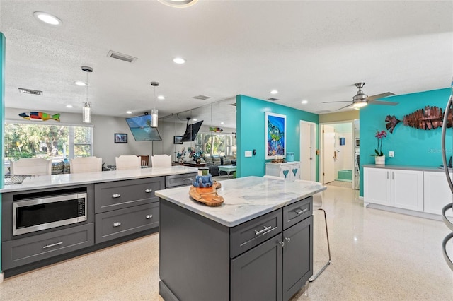 kitchen featuring gray cabinets, a kitchen island, stainless steel microwave, decorative light fixtures, and a textured ceiling