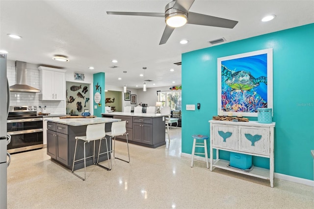 kitchen with a breakfast bar, white cabinetry, double oven range, a center island, and wall chimney range hood