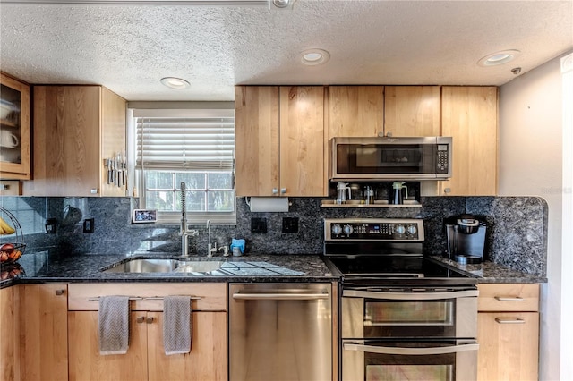 kitchen featuring stainless steel appliances, sink, backsplash, and dark stone counters