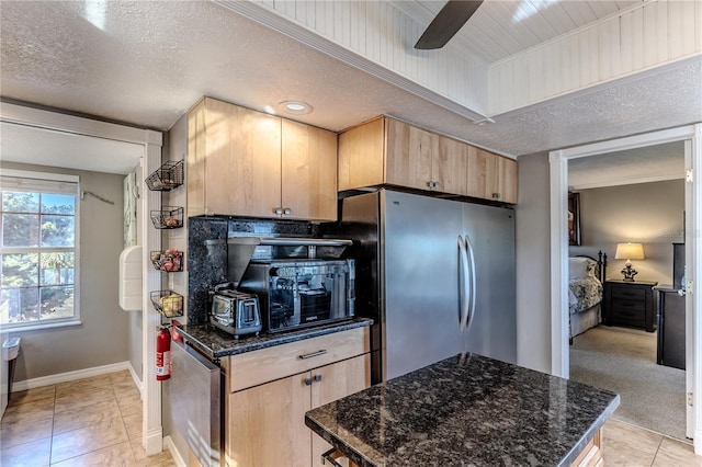 kitchen featuring stainless steel fridge, a textured ceiling, light tile patterned flooring, dark stone counters, and light brown cabinets