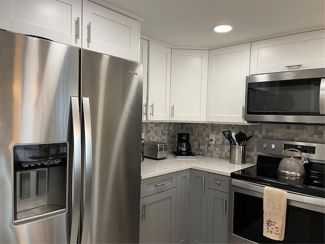 kitchen with white cabinetry, gray cabinets, stainless steel appliances, light stone countertops, and decorative backsplash