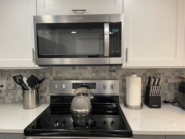 kitchen with white cabinetry, appliances with stainless steel finishes, backsplash, and light stone counters