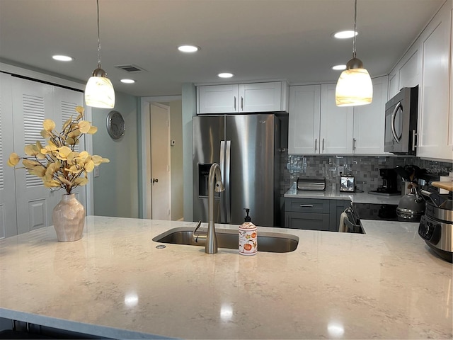 kitchen with tasteful backsplash, stainless steel fridge, decorative light fixtures, and light stone countertops