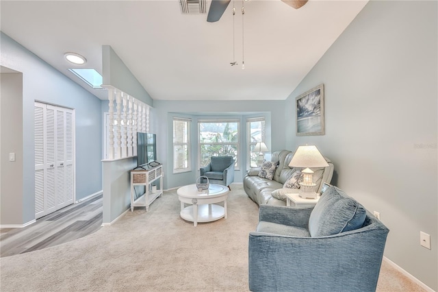 living room with lofted ceiling with skylight, ceiling fan, and carpet