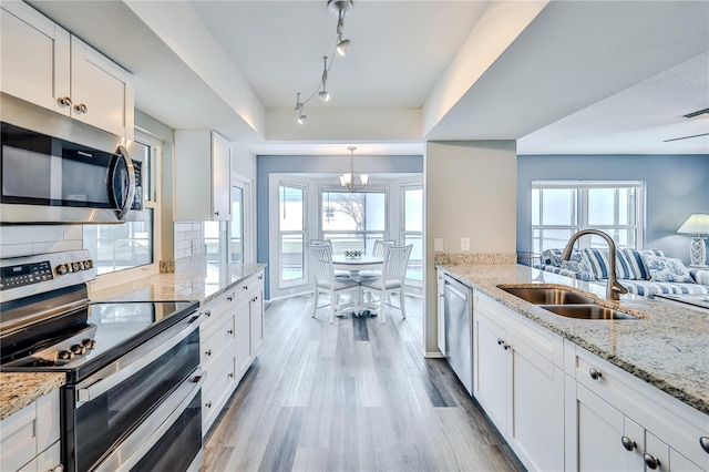 kitchen with sink, white cabinetry, light wood-type flooring, appliances with stainless steel finishes, and light stone countertops