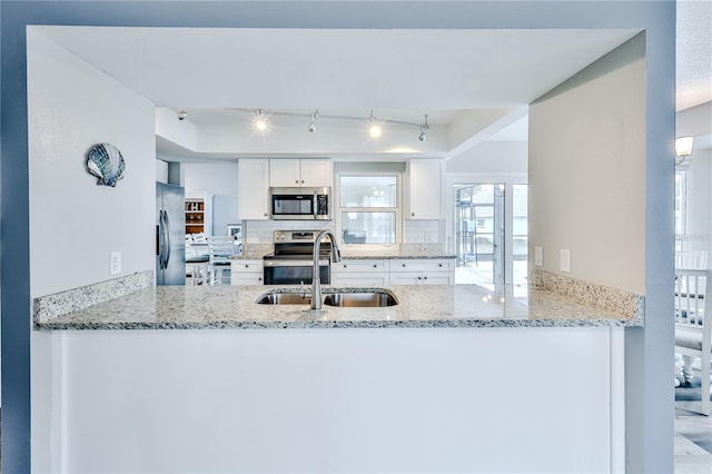 kitchen featuring sink, appliances with stainless steel finishes, kitchen peninsula, light stone countertops, and white cabinets