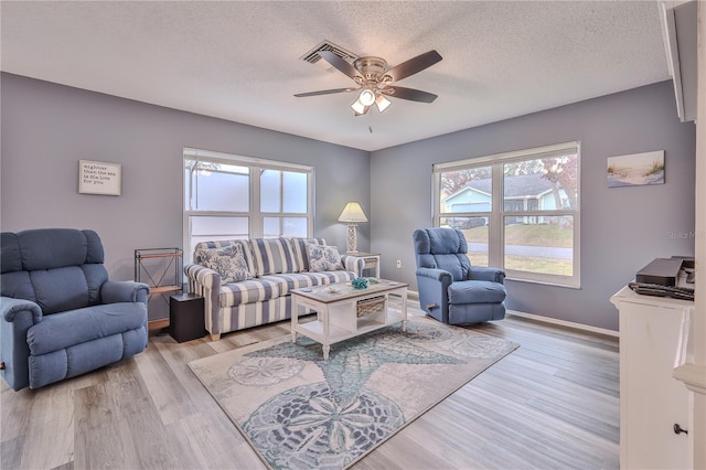 living room with a textured ceiling, ceiling fan, and light hardwood / wood-style flooring