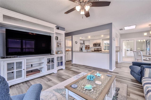 living room with ceiling fan with notable chandelier, light hardwood / wood-style floors, and a textured ceiling