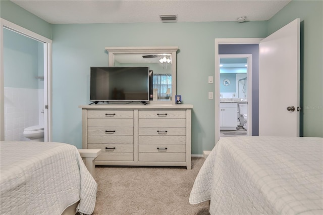 bedroom featuring ensuite bath, tile walls, light carpet, and a textured ceiling