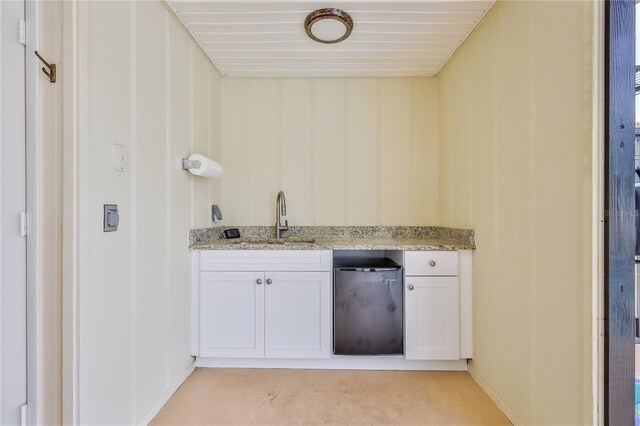 kitchen featuring sink, light stone countertops, stainless steel refrigerator, and white cabinets