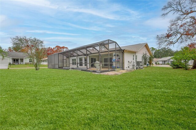 back of property with a lawn, central air condition unit, and glass enclosure