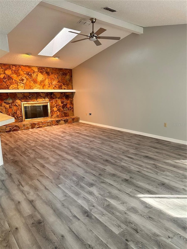 unfurnished living room with hardwood / wood-style floors, a stone fireplace, vaulted ceiling with skylight, and a textured ceiling