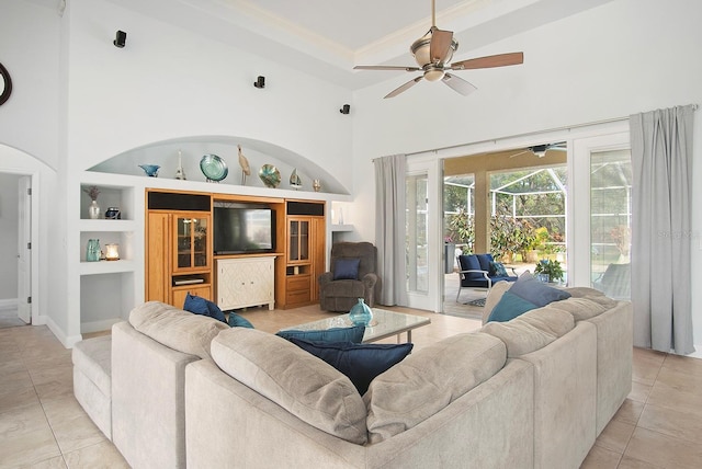 tiled living room with a high ceiling, ornamental molding, ceiling fan, and built in shelves