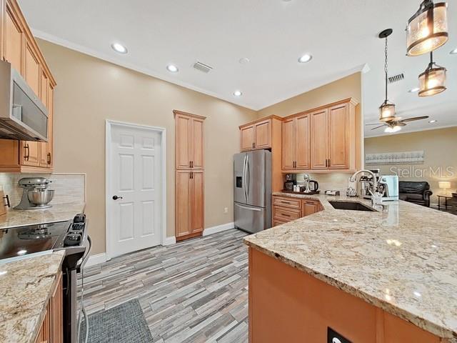 kitchen featuring sink, hanging light fixtures, ceiling fan, light stone counters, and stainless steel appliances