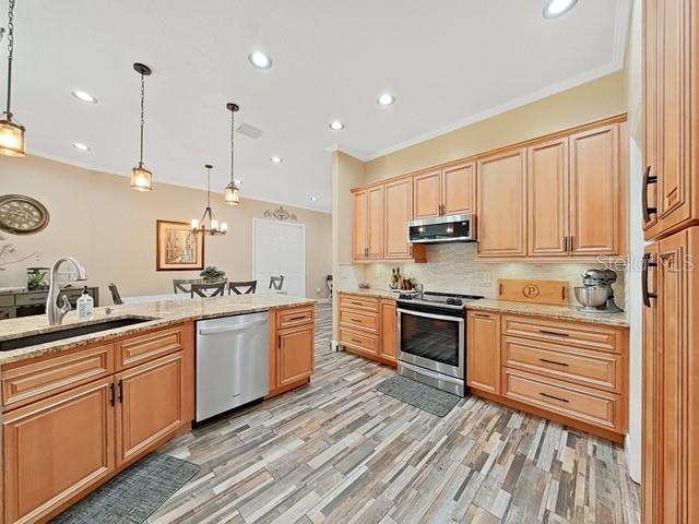 kitchen with decorative light fixtures, sink, decorative backsplash, stainless steel appliances, and light wood-type flooring