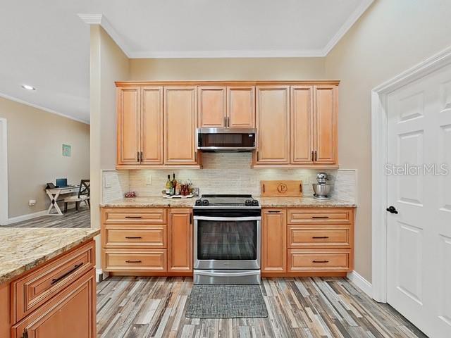 kitchen featuring appliances with stainless steel finishes, tasteful backsplash, light stone countertops, ornamental molding, and light wood-type flooring