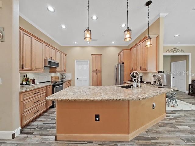 kitchen featuring appliances with stainless steel finishes, decorative light fixtures, sink, kitchen peninsula, and light stone countertops