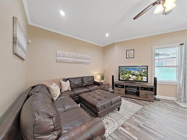 living room featuring ceiling fan, ornamental molding, and light hardwood / wood-style flooring