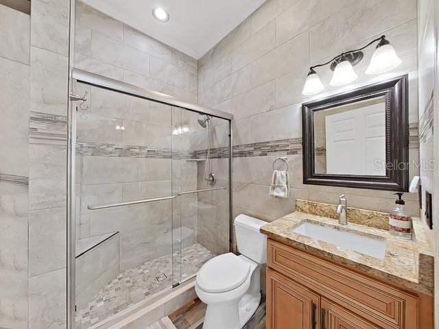 bathroom featuring vanity, a shower with shower door, tile walls, and toilet