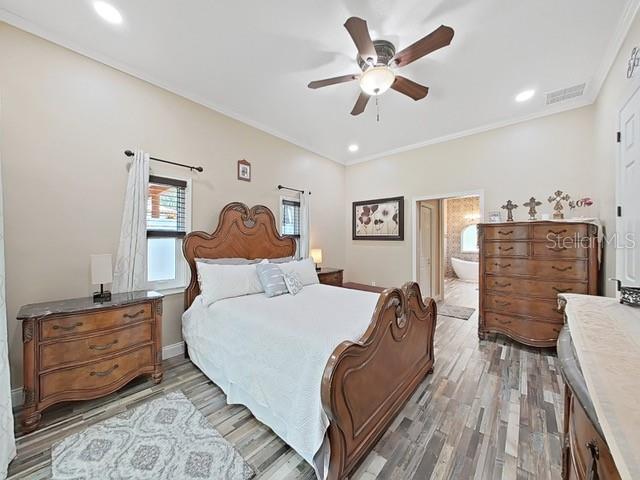 bedroom with connected bathroom, hardwood / wood-style flooring, ornamental molding, and ceiling fan