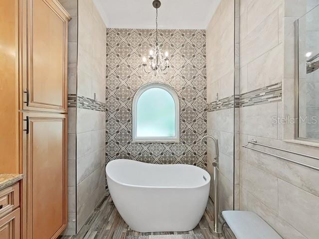 bathroom featuring a bath, vanity, tile walls, and a notable chandelier