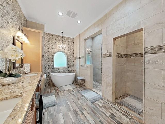 bathroom with tile walls, hardwood / wood-style floors, vanity, a notable chandelier, and plus walk in shower