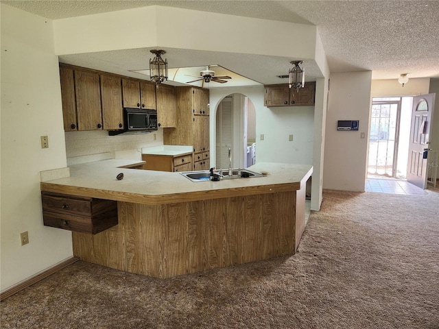 kitchen featuring light colored carpet, a sink, a textured ceiling, black microwave, and a peninsula